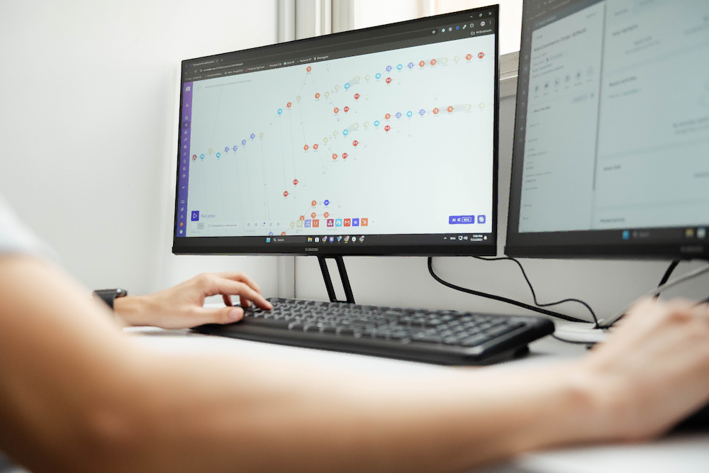 Person analyzing data on dual monitors with graphs and charts, illustrating automation in business.